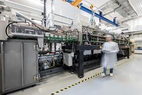 Verschwommener Mann in Laborkleidung läuft an Beschichtungsanlage des ZSW vorbei.